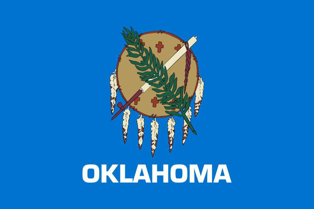 The Oklahoma state flag, displaying a traditional Osage Nation buffalo-skin shield with seven eagle feathers, crossed by a ceremonial pipe and an olive branch. The word 'OKLAHOMA' appears in white capital letters on a blue background.